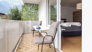 Ein Balkon mit Tisch und Stühlen, ein Bett mit Kissen und Blick auf Berge.
