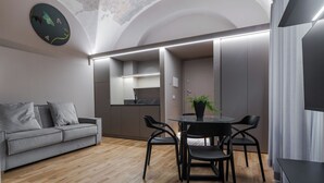 Un interior moderno con un sofá gris, una mesa de comedor redonda con sillas y una cocina con armarios y encimera.