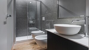Un baño moderno con ducha envuelta en vidrio, un lavabo grande de color blanco y un mueble de tocador en tonos oscuros.
