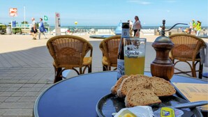 Una mesa con una botella de Blanquette de Narque, una cerveza y rebanadas de pan en una terraza frente al mar.