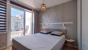 Un dormitorio con una cama grande, una mesita de noche pequeña, un lámpara colgante y vistas al exterior a través de una ventana.