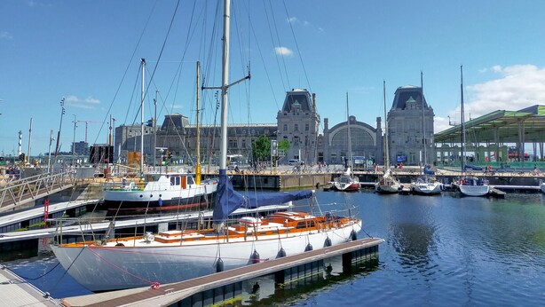 Un puerto deportivo con barcos amarrados, un edificio grande con cúpula al fondo y una zona cubierta con techo verde.