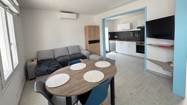 A modern, compact living space with a dining area, kitchenette, and a TV mounted on the wall.
