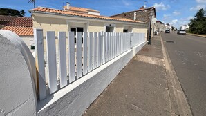 A street with a white fence, a building with a tiled roof, and a clear blue sky.