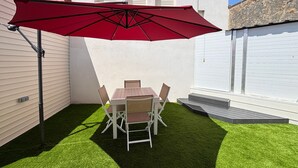 A patio with a table and chairs, a red umbrella, and artificial grass.