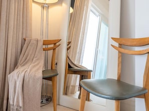 A room with a wooden chair, a floor lamp, and a mirror reflecting the room.