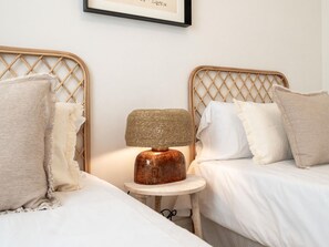 A room with two beds, a round wooden table with a lamp, and a framed picture on the wall.