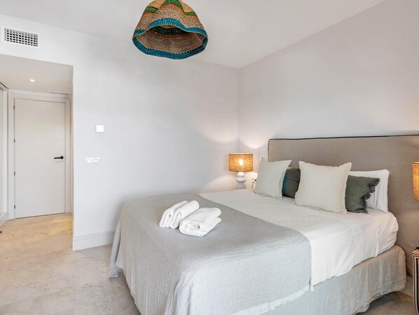 A bedroom with a bed, a bedside lamp, and a hanging light fixture.