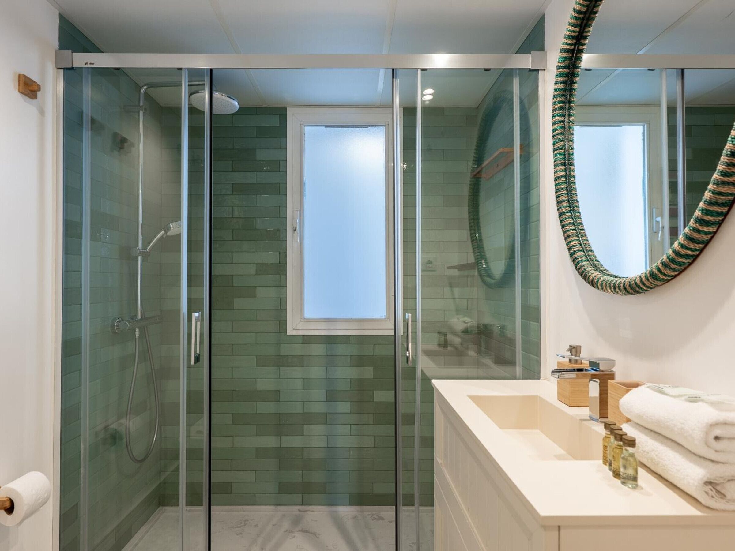 Un baño moderno con cabina de ducha de vidrio, un espejo grande y tocador con artículos de aseo.
