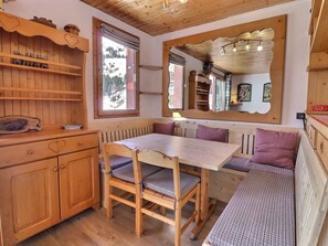 Interior acogedor de una cabaña con una mesa de comedor de madera, asientos tipo banco y un espejo grande que refleja la habitación.