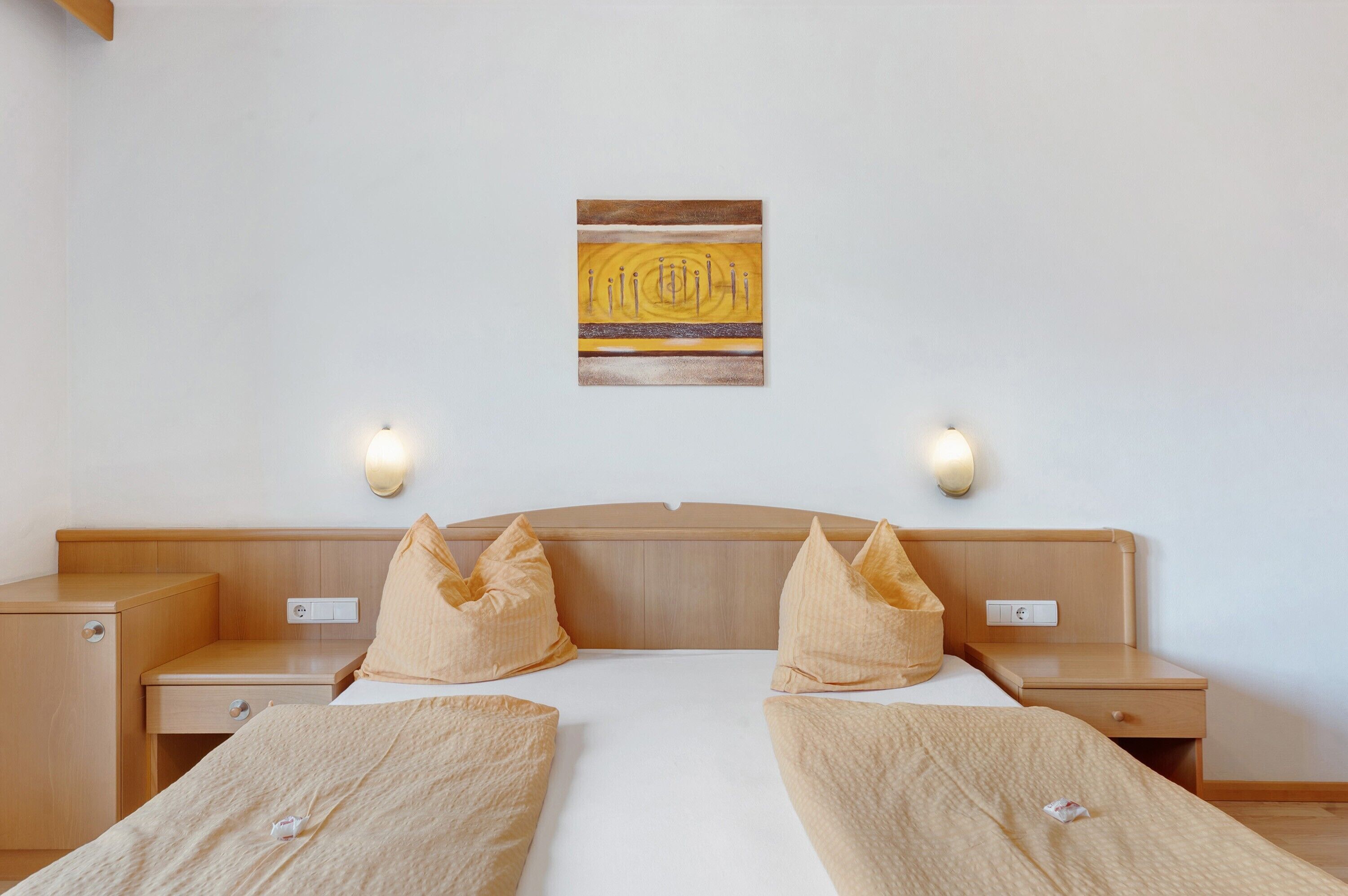 Habitación de hotel con cama, dos mesitas de noche, una obra de arte colgada en la pared y dos luces empotradas.