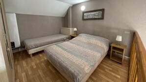 A bedroom with two single beds, a wooden floor, a ceiling light, and a framed picture on the wall.