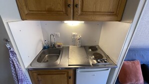 A compact kitchenette with wooden cabinets, a stainless steel sink, a stove, and a small refrigerator.
