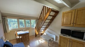 A cozy living room with a wooden staircase, a dining area, and wooden cabinets.