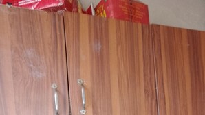 Un meuble en bois avec des poignées en métal, un sol carrelé et un paquet rouge, partiellement visible, posé sur le dessus.
