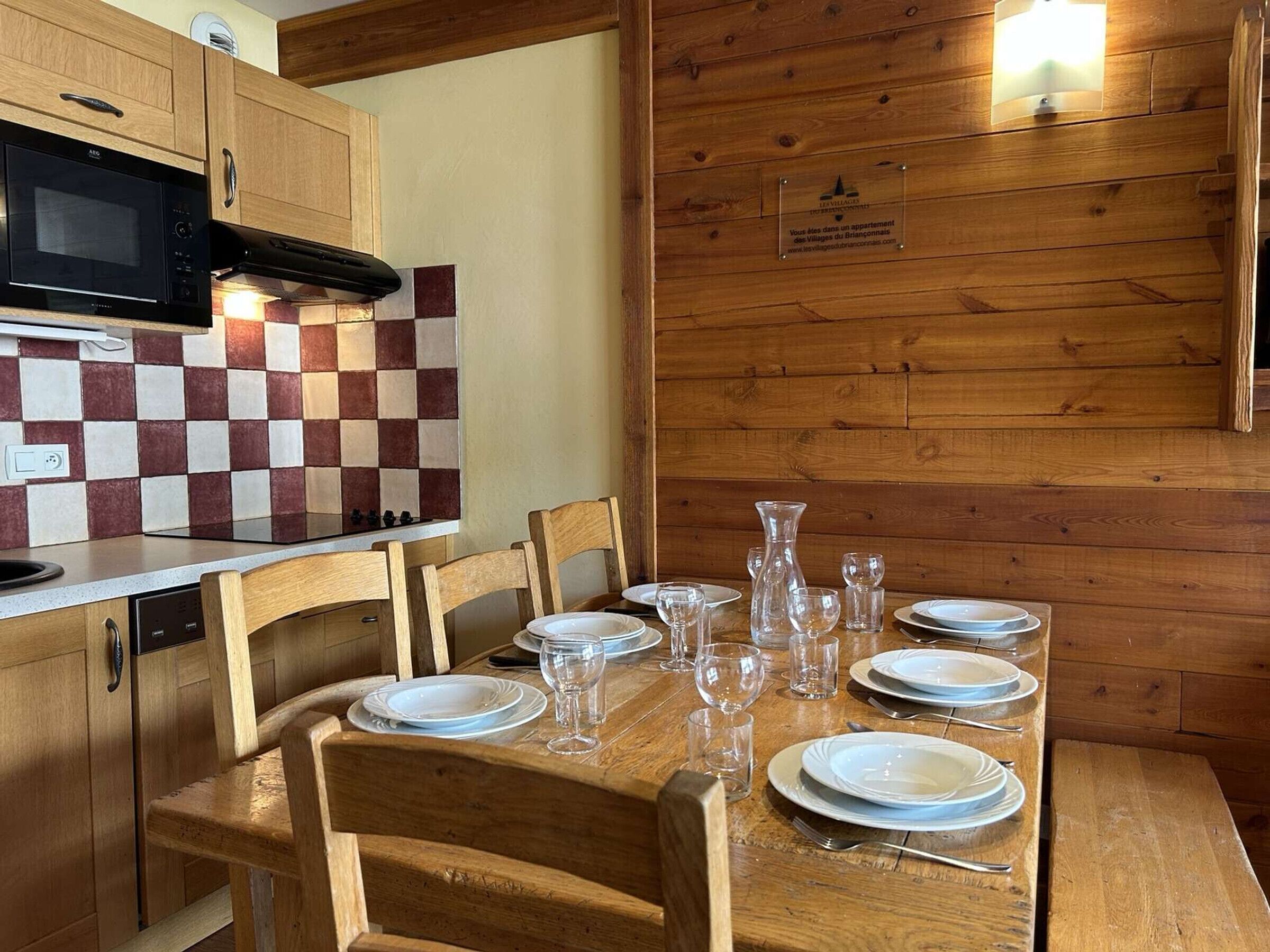 Un intérieur en bois agrémenté d’un pare-feu à carreaux, d’un four à micro-ondes et d’une table à manger mise avec des assiettes et des verres.