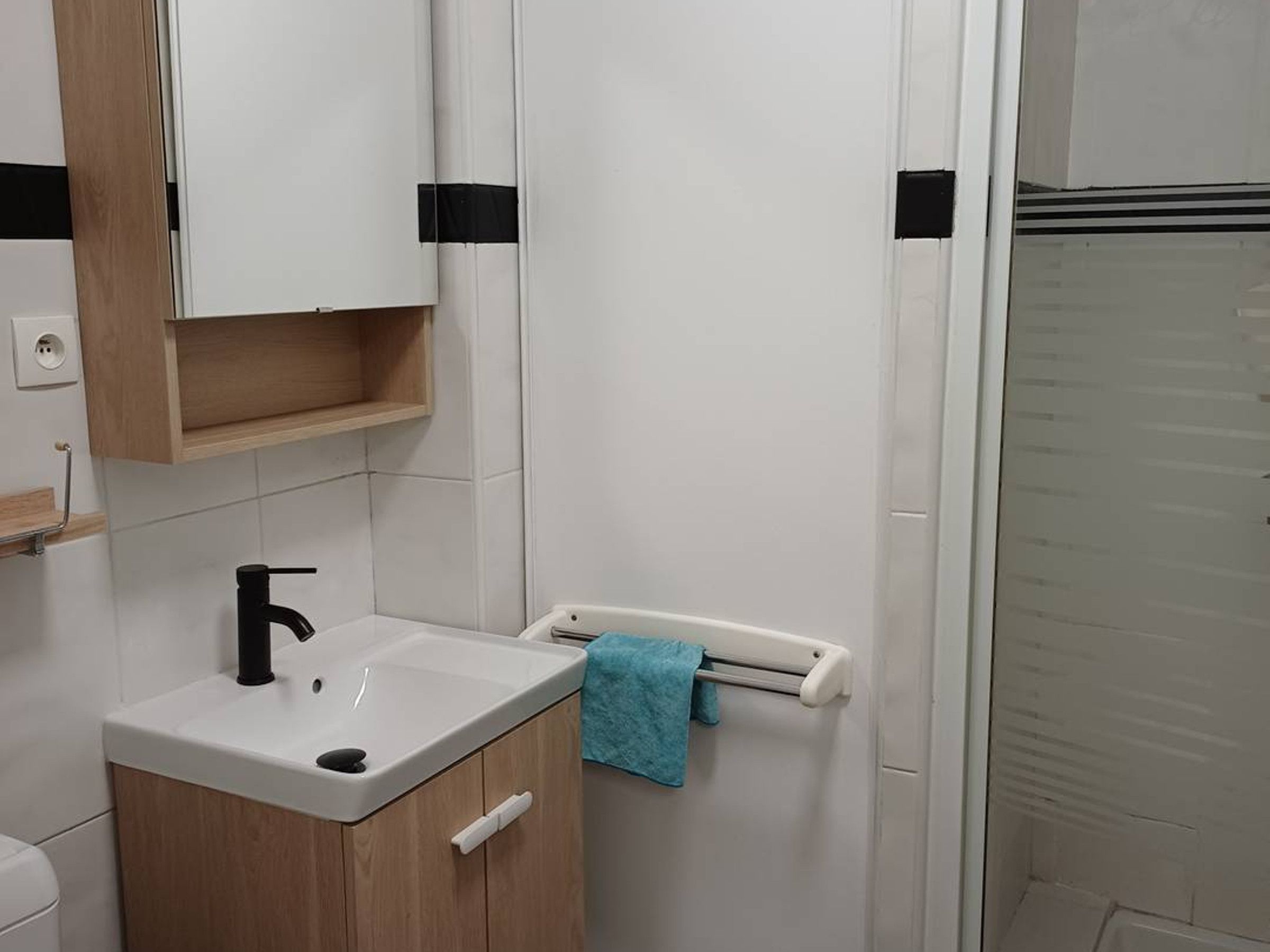 A bathroom with a white sink, a mirror, a wooden cabinet, and a towel rack.