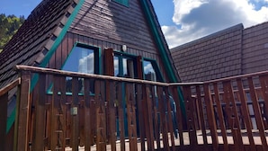 Una baita di legno con tetto a forte pendenza, ampie finestre e una veranda in legno con ringhiera.
