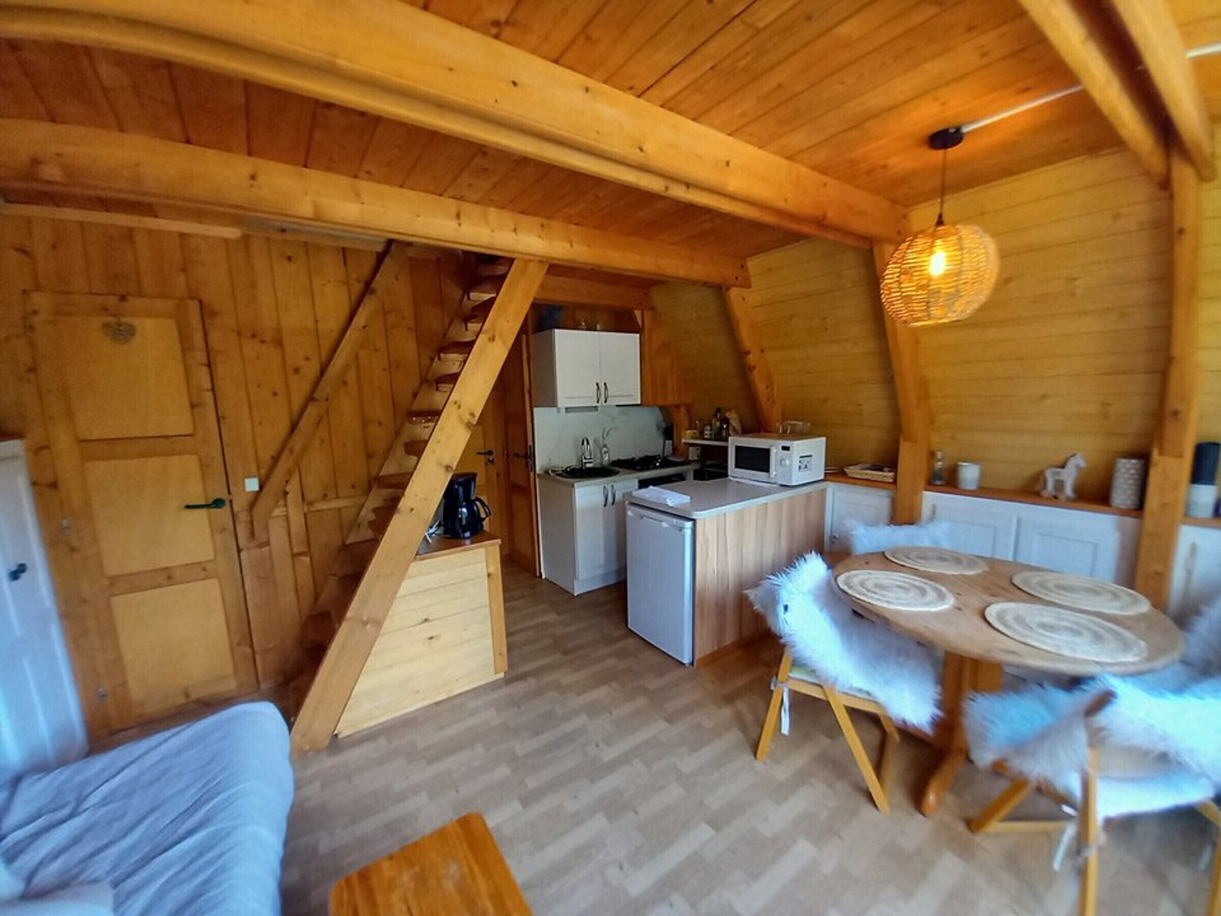 A cozy attic-style room with a wooden staircase, a kitchenette, a dining area with a round table and chairs, and a sofa.