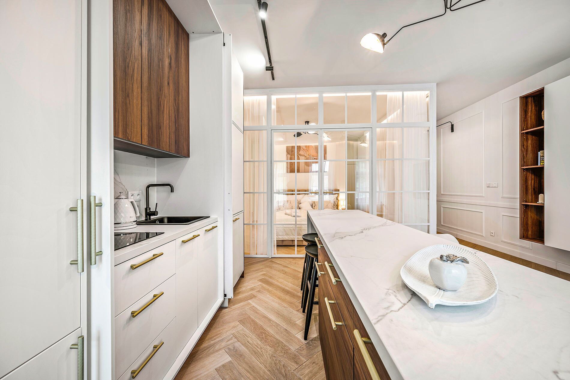Una cocina moderna con armarios blancos, encimera de mármol y vistas al dormitorio contiguo.