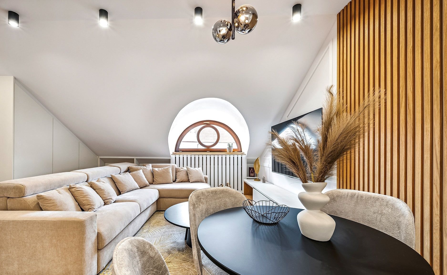 Ein modernes Wohnzimmer mit einer Eckcouch, einem runden Couchtisch und einem Essbereich mit einem schwarzen Tisch und weißen Stühlen.