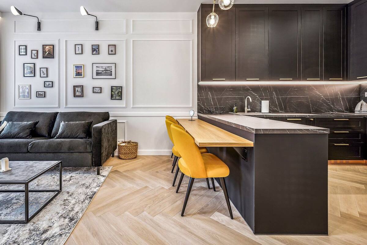 Una cocina moderna con armarios oscuros, salpicadero de mármol y una mesa de comedor de madera con sillas amarillas.