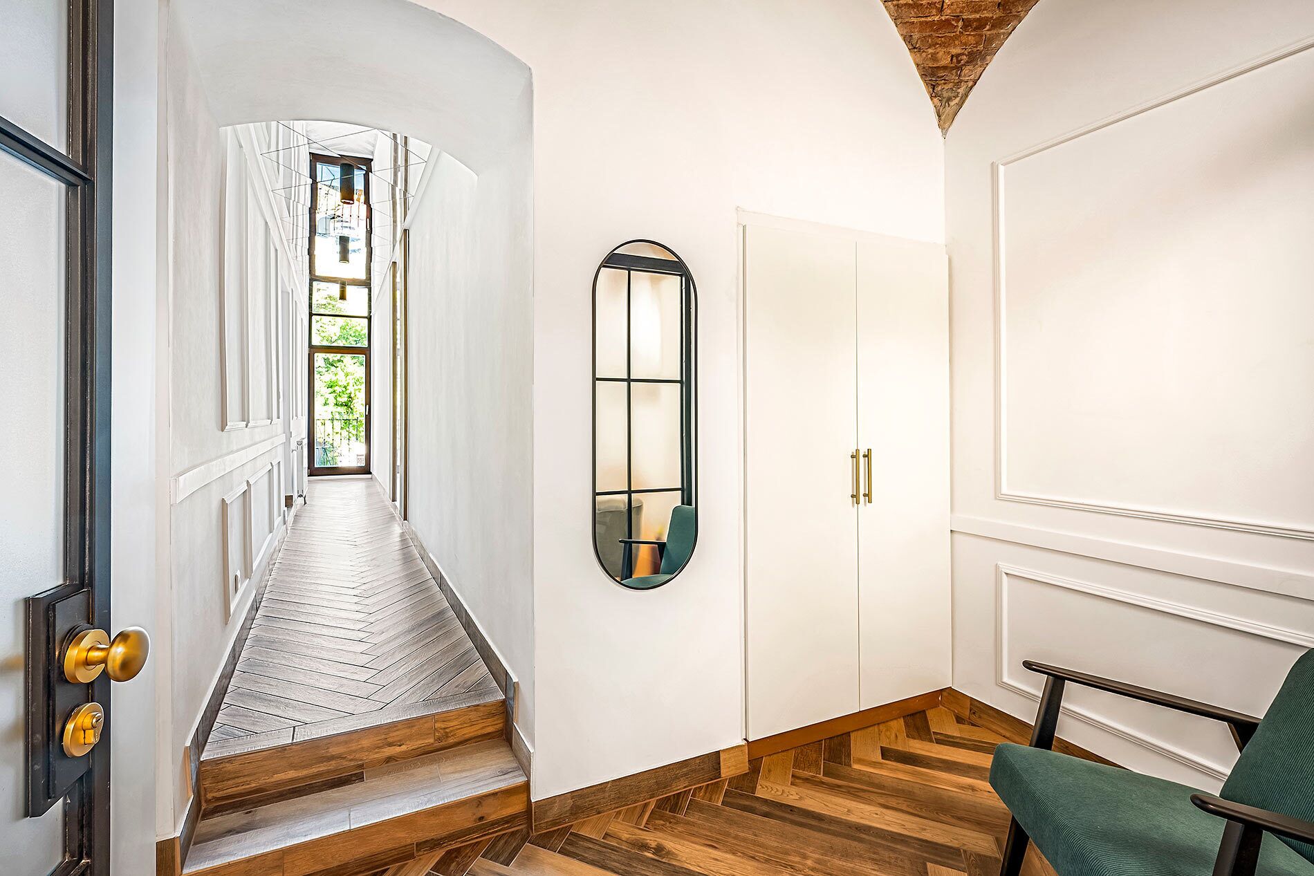 A hallway with a wooden staircase, a mirror, and a green chair.