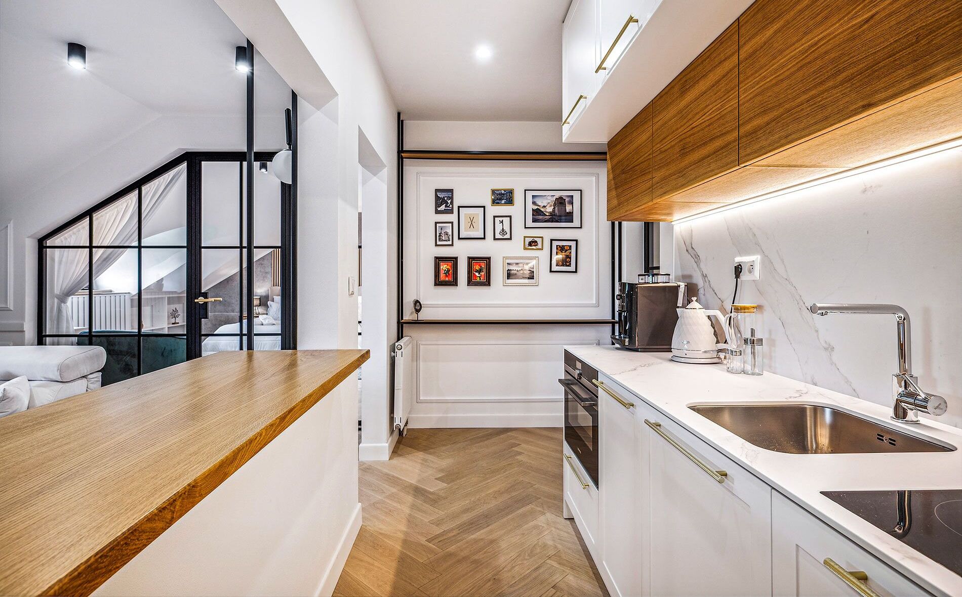 Una cucina moderna con piano di lavoro in legno, mobili bianchi e schienale in marmo. C'è una zona pranzo con tavolo e sedie bianche e una scala che conduce a un piano superiore.