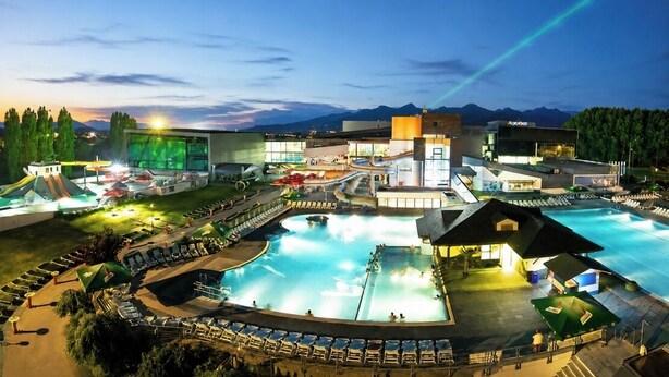 Et resort med en stor swimmingpool, flere bygninger og et bjergrigt landskab i baggrunden.