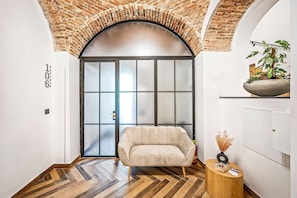 A modern interior with a herringbone wood floor, a beige sofa, a wooden side table, and a brick archway. - Beňovský Apartments (Poprad)