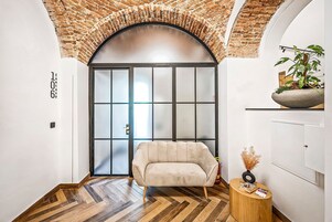 Un interior moderno con suelo de madera en patrón de espiga, un sofá beige, una mesita de madera y un arco de ladrillo.