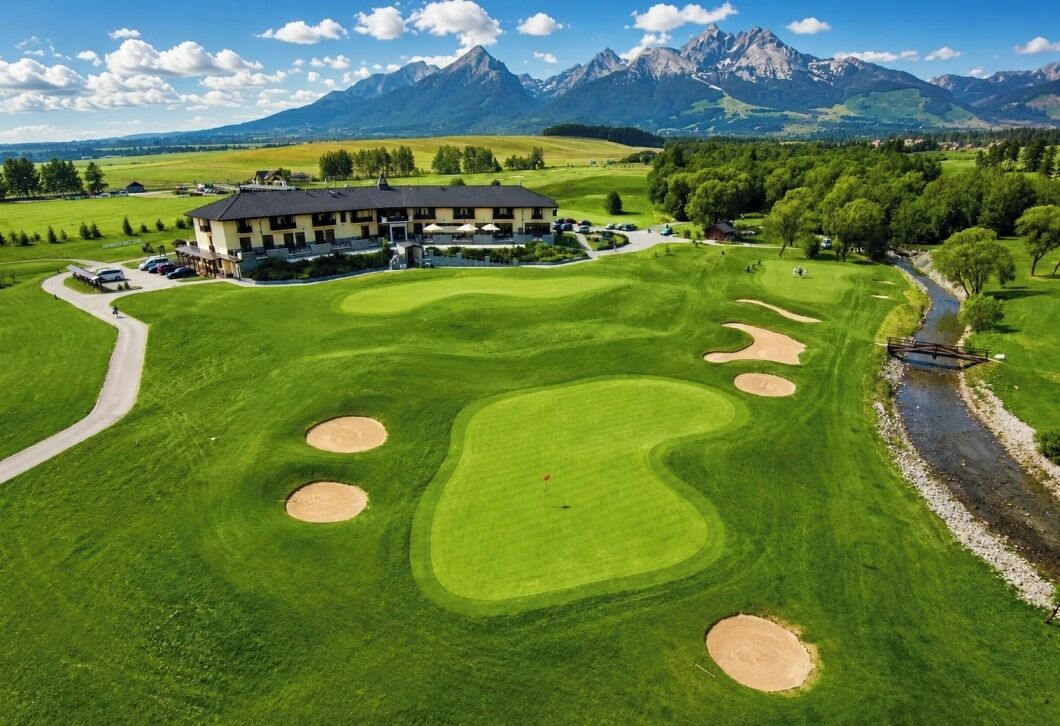 A golf course with bunkers, a clubhouse, and a mountain backdrop.