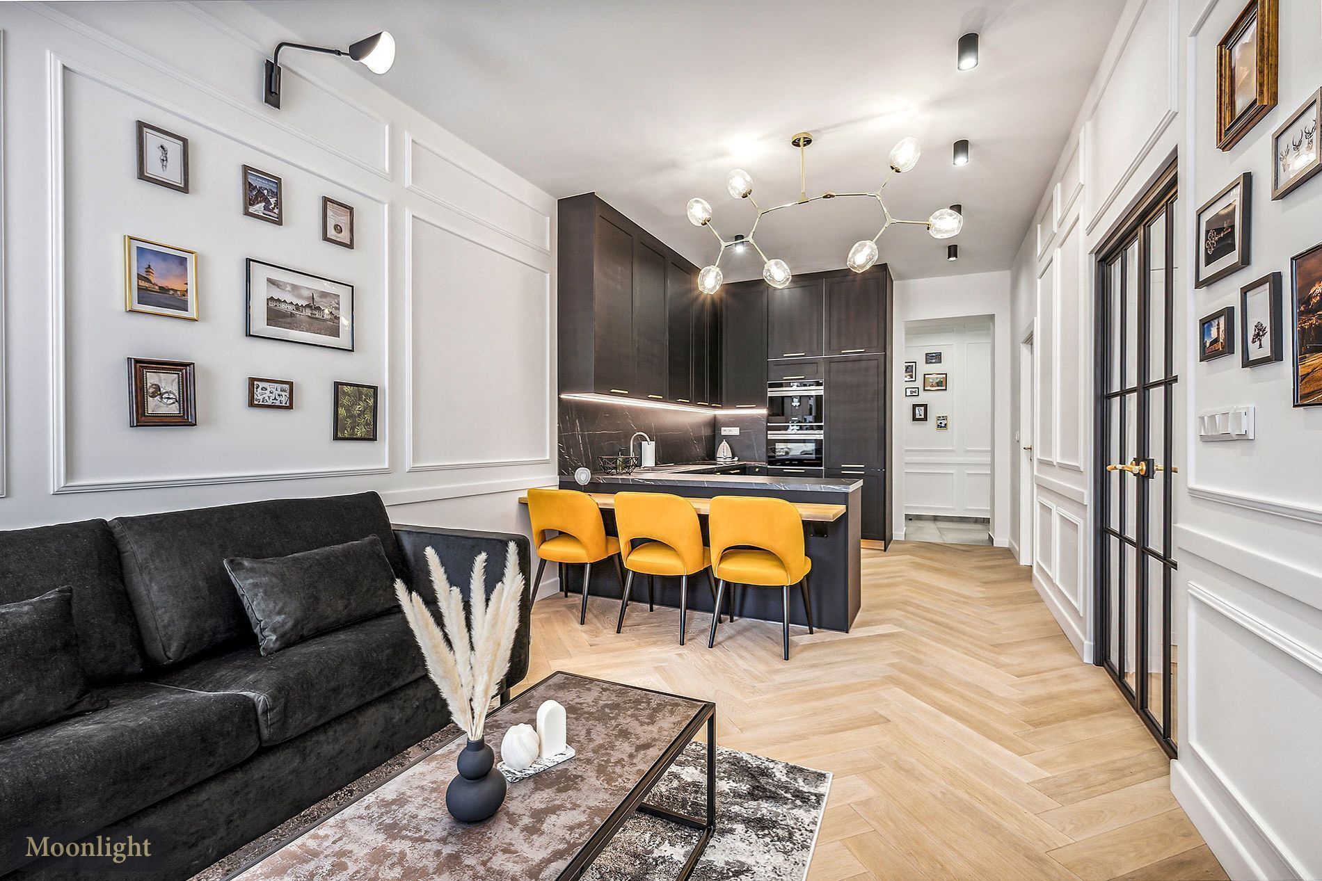 A modern living room with a dark sofa, a coffee table with a vase and decorative items, and a bright yellow dining area with chairs.
