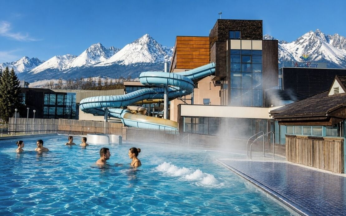 Una piscina con tobogán de agua, un paisaje montañoso de fondo y un edificio con un cartel que dice 'AOC City'.