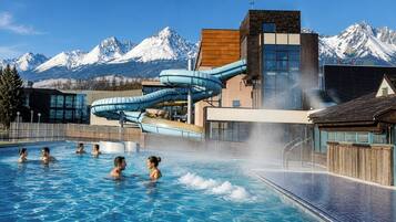 Una piscina con tobogán de agua, un paisaje montañoso de fondo y un edificio con un cartel que dice 'AOC City'.