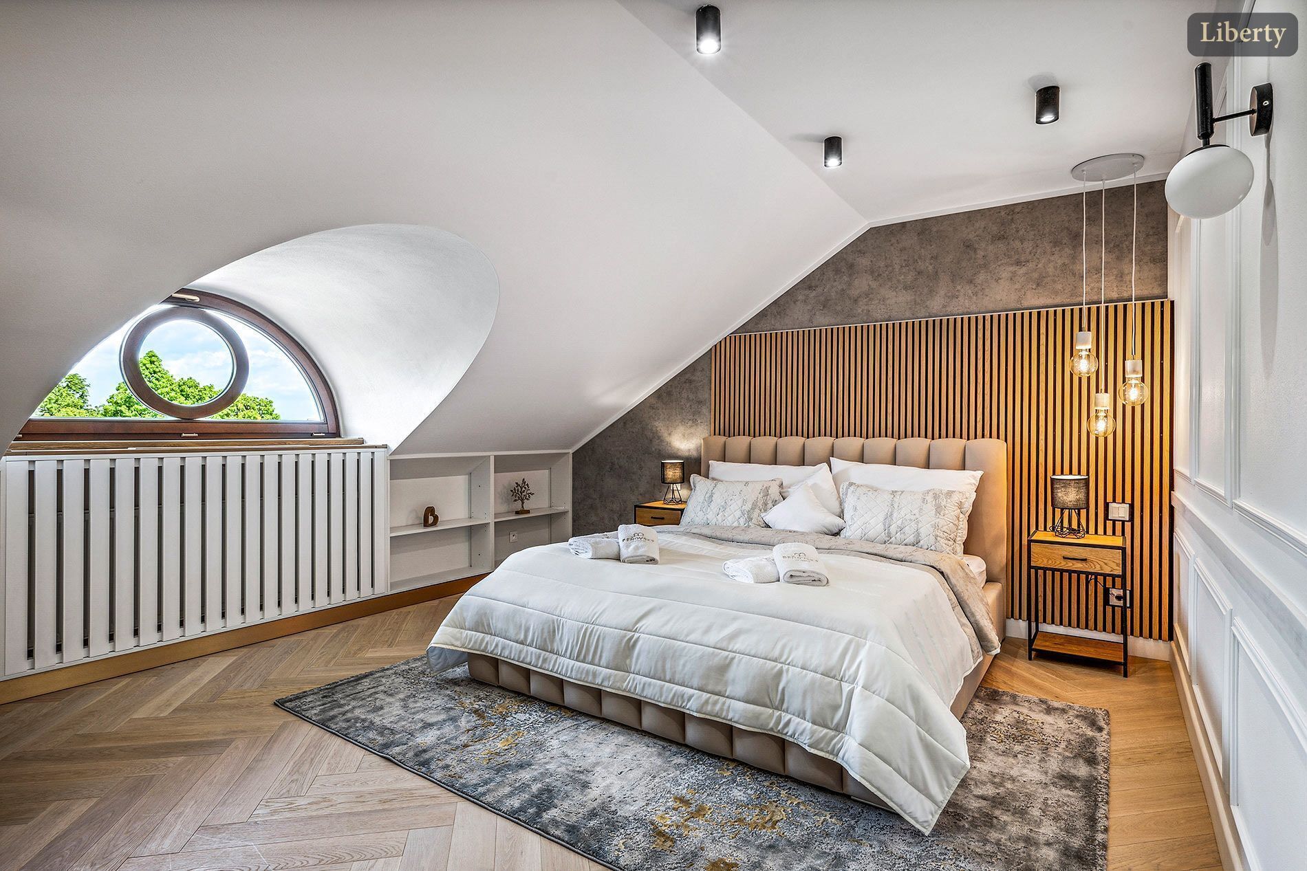 A modern bedroom with a sloped ceiling, a large bed, bedside tables, and a view through a skylight.