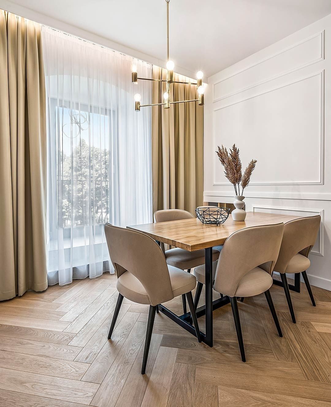 A dining area with a wooden table, six chairs, a vase with dried plants, and a modern chandelier.