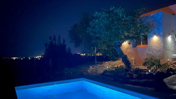 A nighttime view of a swimming pool area with a tree and a building illuminated by lights.