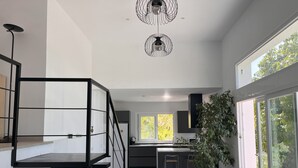 A modern kitchen with a central island, a dining area with a round table, and a staircase with a black railing.