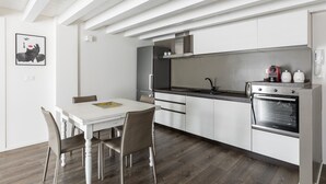 A modern kitchen with white cabinetry, a black countertop, and stainless steel appliances. There is a dining table with chairs and a framed picture on the wall. - Casa del Borgo by Wonderful Italy (Bologna)