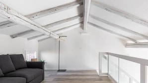 A loft-style room with exposed wooden beams, a dark gray sofa, and a modern floor lamp. - Casa del Borgo by Wonderful Italy (Bologna)