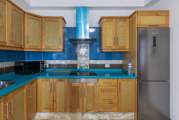 Une cuisine avec des meubles de rangement en bois, un réfrigérateur en acier inoxydable, un four à micro-ondes et un plan de travail bleu.