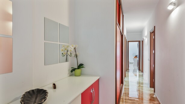 Un pasillo con pared blanca, una orquídea en maceta, un cuenco decorativo y un mueble de color rojo.