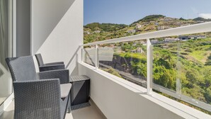 Un balcon avec des fauteuils en osier et une vue sur un paysage vallonné parsemé de bâtiments.