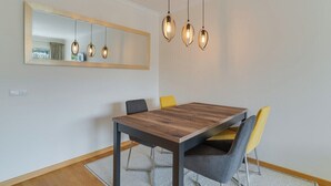 Un coin repas avec une table en bois, quatre chaises, un luminaire suspendu et un grand miroir au mur.