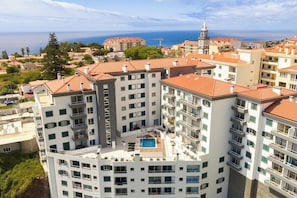 A multi-story hotel with a rooftop pool, surrounded by other buildings and a view of the sea.
