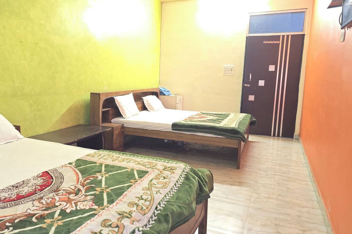 A hotel room with two beds, a wooden headboard, a nightstand, a green patterned bedspread, and a yellow wall.
