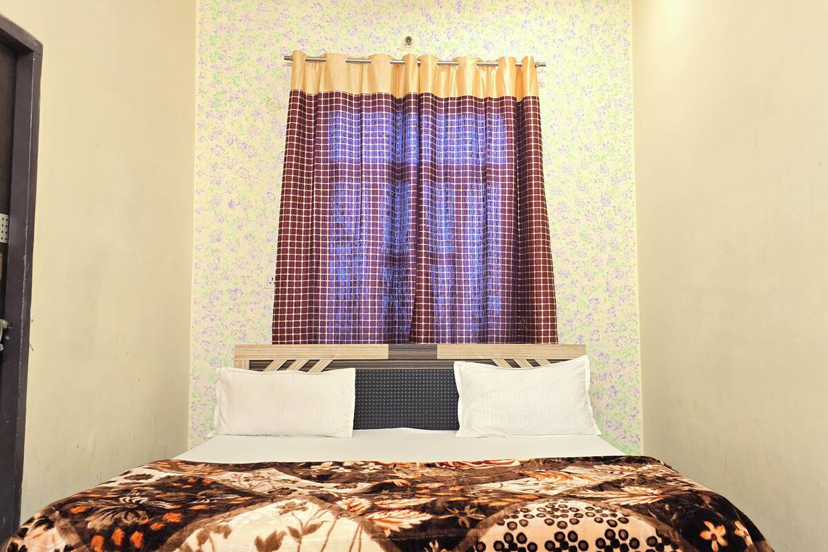 A bedroom with a bed, a window with patterned curtains, and a door with a handle.