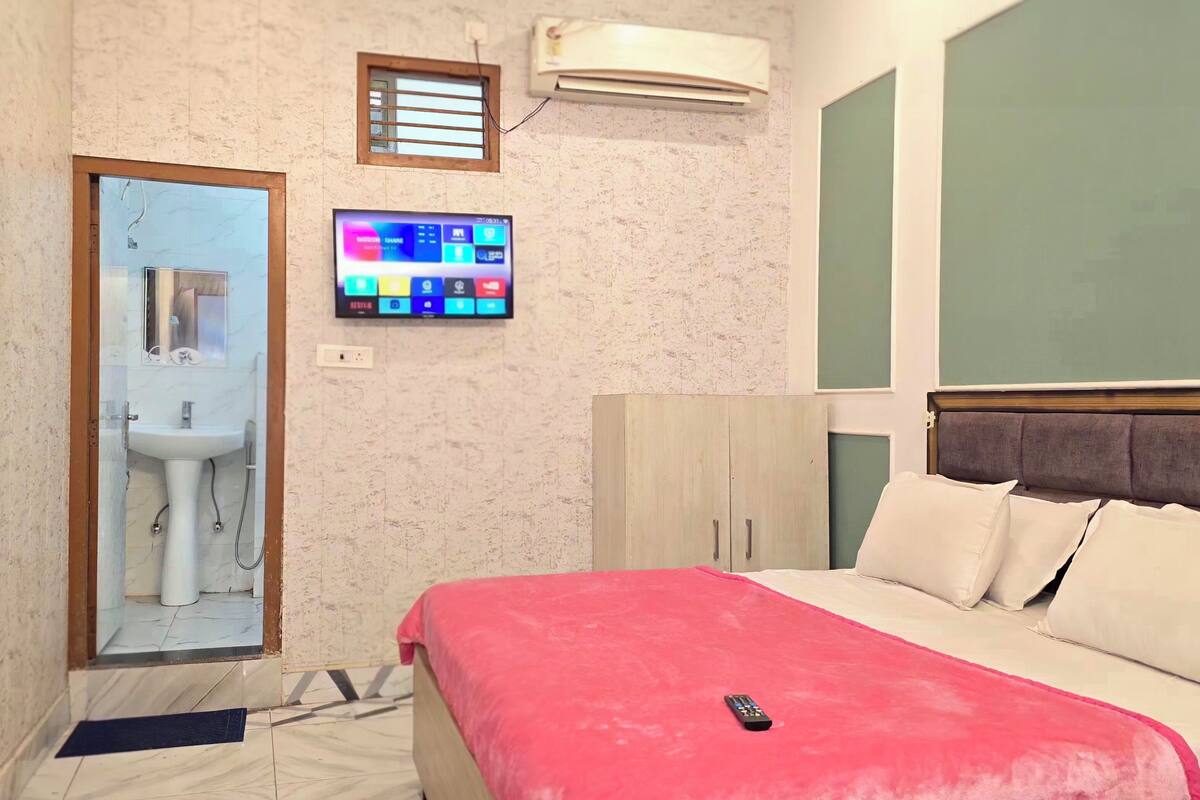 A hotel room with a bed, a TV mounted on the wall, a wardrobe, and a bathroom visible through an open door.