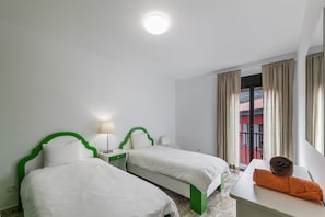 Une chambre d’hôtel avec deux lits, une table de chevet avec une lampe, une fenêtre avec des rideaux et une vue sur un bâtiment rouge.